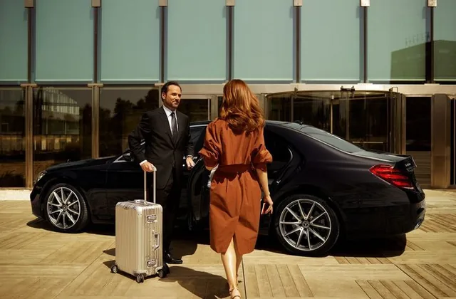 Chauffeur greeting a traveler with luggage beside a luxury black sedan at the airport